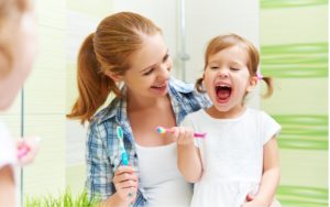 A picture containing person holding a happy child with a toothbrush in hand