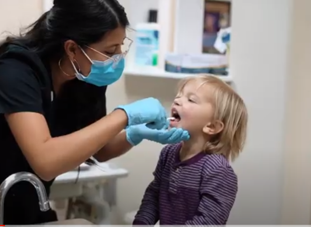 A person in a mask giving a child a dental check