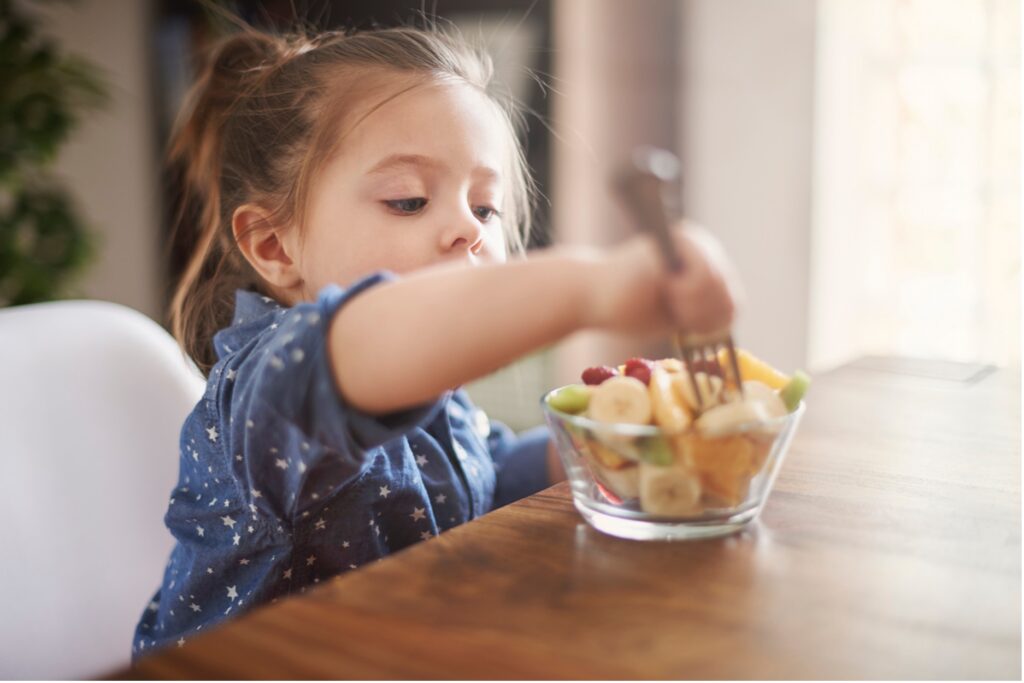 A young child eating a bowl of fruit, how sugar affects children's teeth